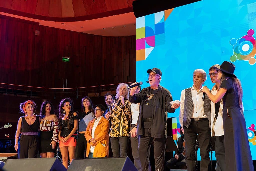 Los artistas del concierto cantan juntos en el escenario, frente a la pantalla con la identidad del Foro.