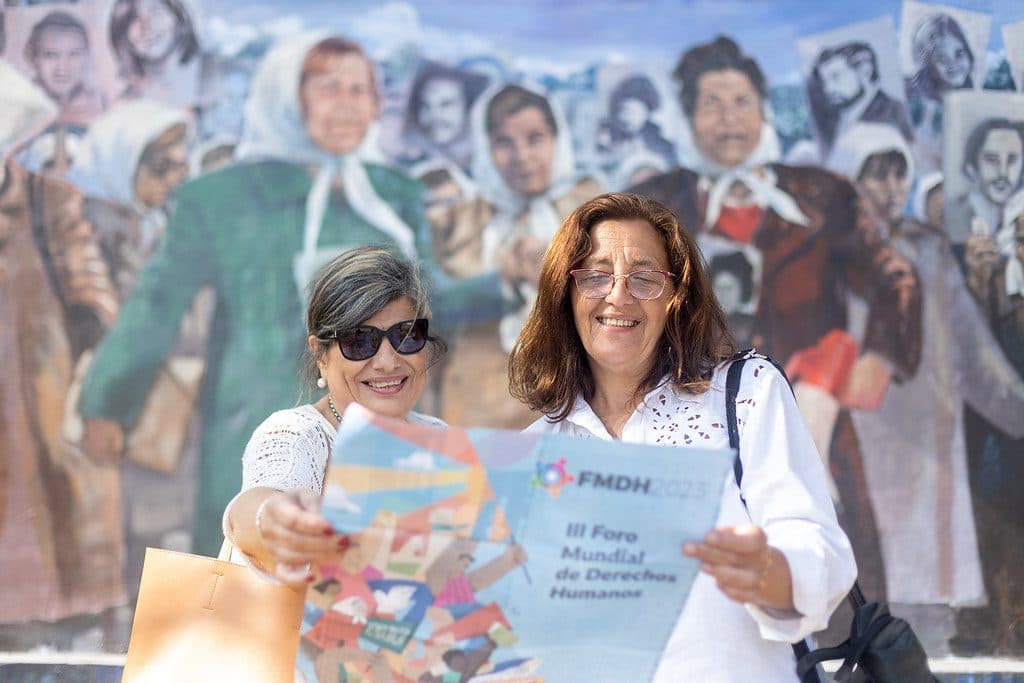 Dos mujeres leen el programa del III Foro Mundial de Derechos Humanos frente a un mural de las Madres de Plaza de Mayo.