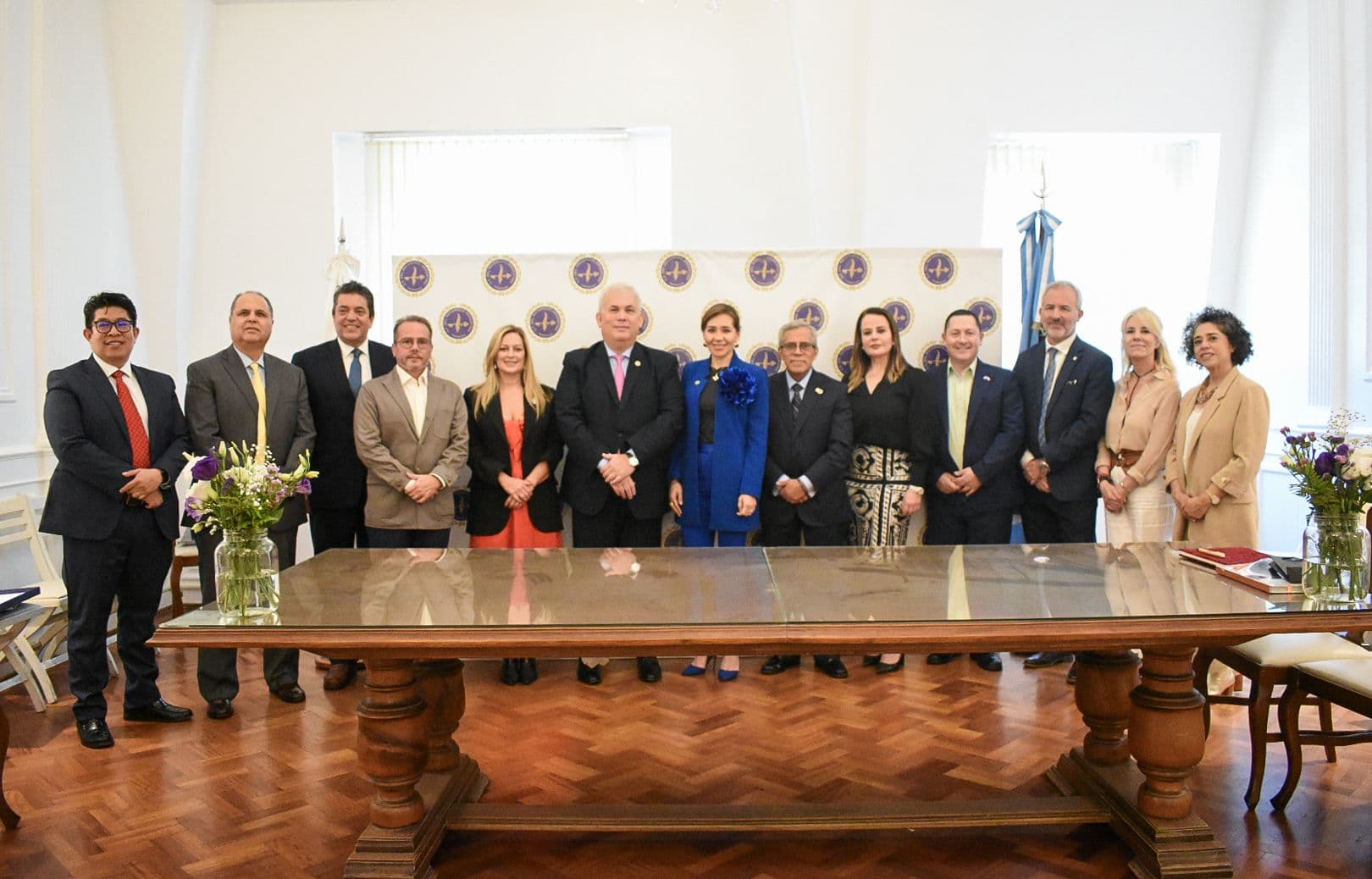 Autoridades del CFNA y una delegación internacional posan detrás de una larga mesa de madera, con las banderas y el telón institucional del Consejo de fondo.