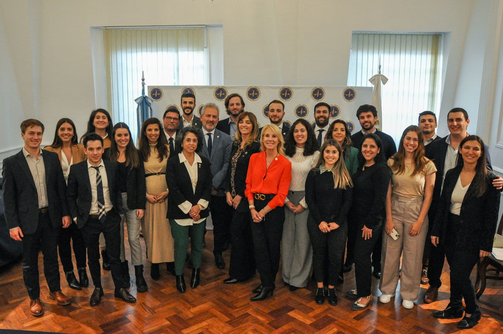 Foto de grupo numerosa en un salón de piso de parquet, frente al telón del CFNA.