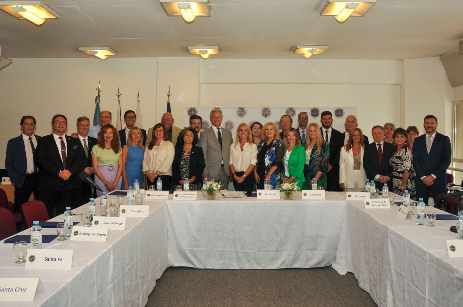 Foto de grupo de un plenario federal: los representantes de los colegios, de pie detrás de la mesa en U con el cartel de cada provincia.