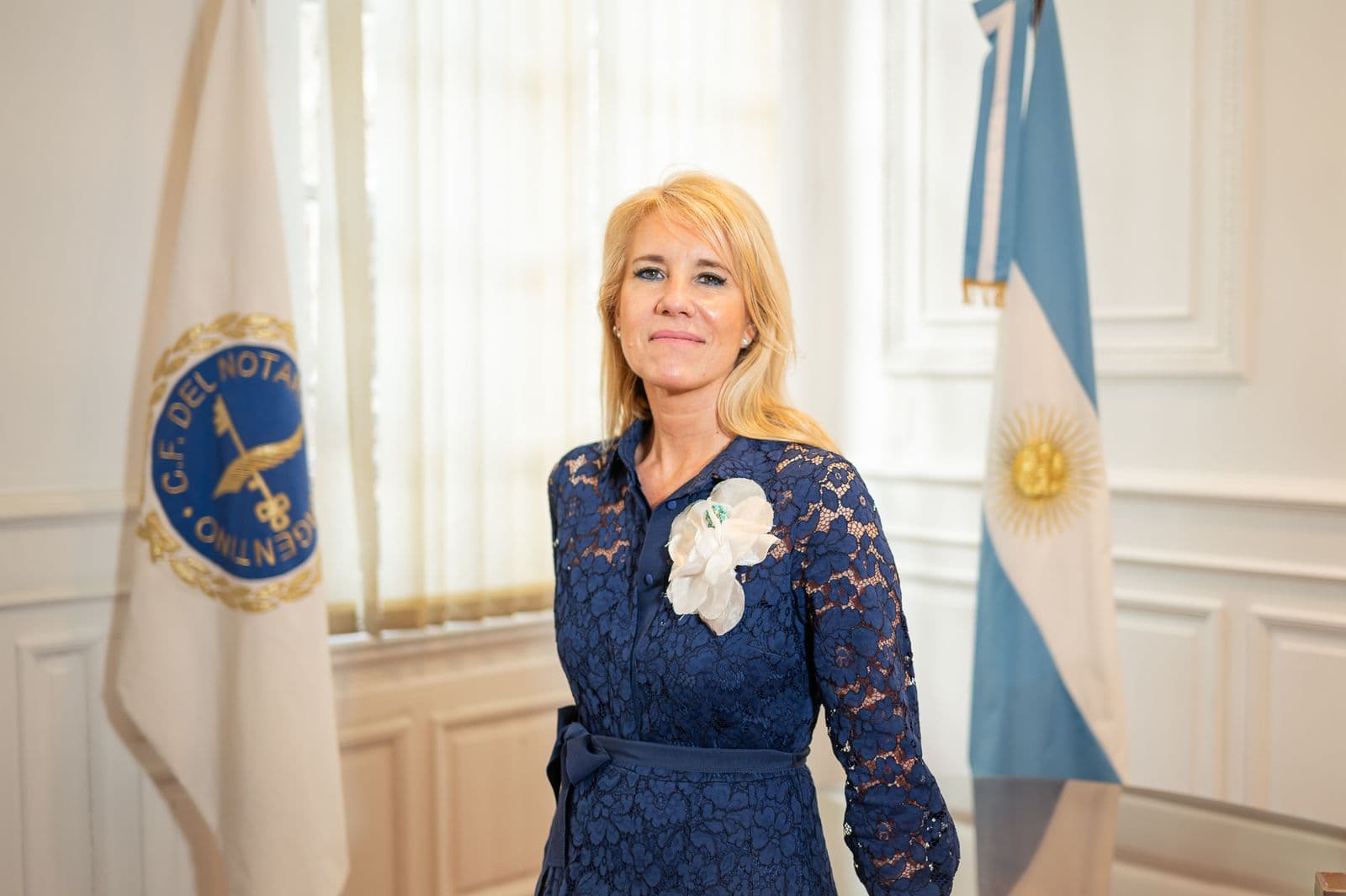 Retrato de una autoridad del Consejo, de pie entre la bandera del CFNA y la bandera argentina.