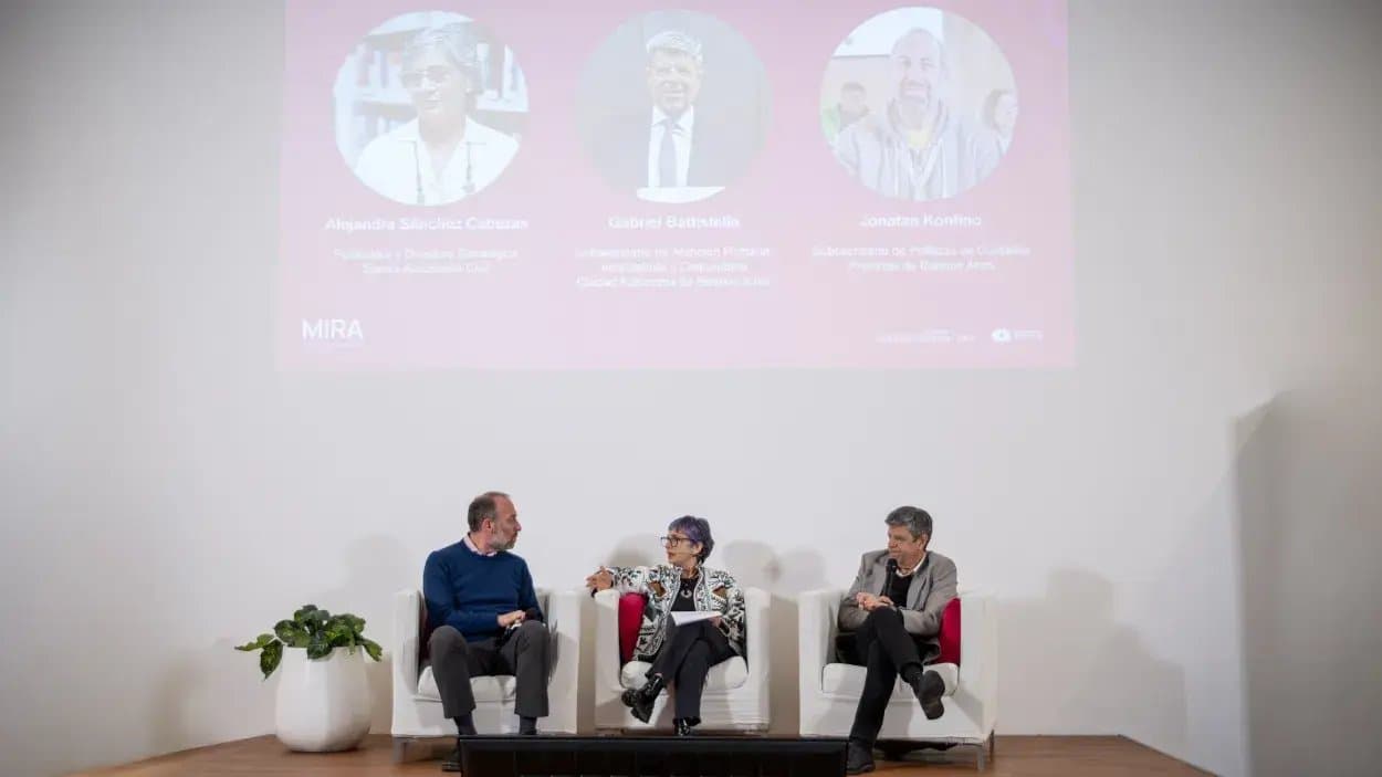 Tres panelistas conversan en sillones blancos sobre un escenario, en la presentación de MIRA. En la pantalla, las fotos y los cargos de Alejandra Sánchez Cabezas, fundadora y directora estratégica de Surcos; Gabriel Battistella, subsecretario de Atención Primaria, Ambulatoria y Comunitaria de la Ciudad de Buenos Aires, y Jonatan Konfino, subsecretario de Políticas de Cuidado de la Provincia de Buenos Aires.